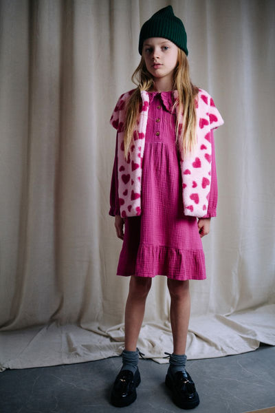 Roze teddy bodywarmer voor meisjes van Daily Brat met rode hartjesprint, mouwloos en zacht gevoerd, ideaal om over een jurk of trui te dragen.