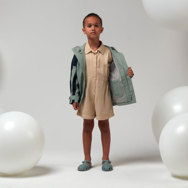 Lichtgroene uniseks regenjas 'Roaring Cat' van Gosoaky met kap en reflecterende strip. | Verkrijgbaar bij Little Fashion Addict