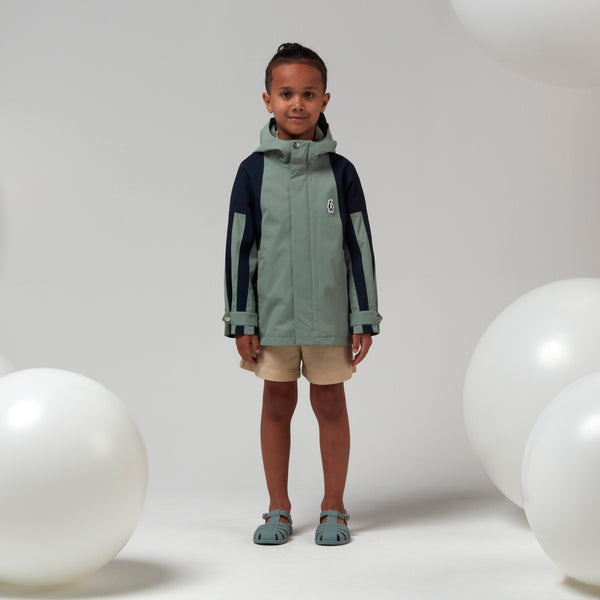 Lichtgroene uniseks regenjas 'Roaring Cat' van Gosoaky met kap en reflecterende strip. | Verkrijgbaar bij Little Fashion Addict