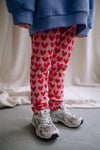 Roze legging van Daily Brat met rode hartjes, gemaakt van biologisch katoen en stretch – perfect voor school en speelplezier.