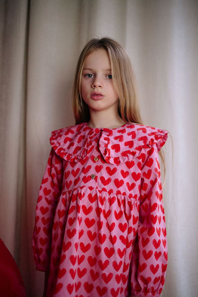 Roze Adore jurk met rode hartjesprint van Daily Brat, met rucheskraag en lange mouwen – gemaakt van biologisch katoen.
