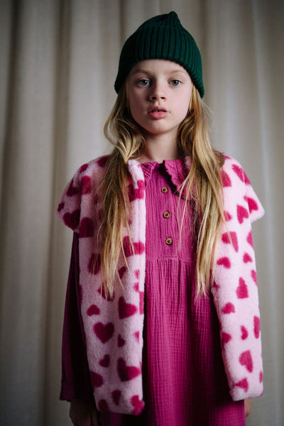 Roze teddy bodywarmer voor meisjes van Daily Brat met rode hartjesprint, mouwloos en zacht gevoerd, ideaal om over een jurk of trui te dragen.