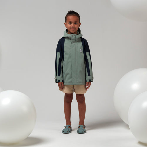 Lichtgroene uniseks regenjas 'Roaring Cat' van Gosoaky met kap en reflecterende strip. | Verkrijgbaar bij Little Fashion Addict